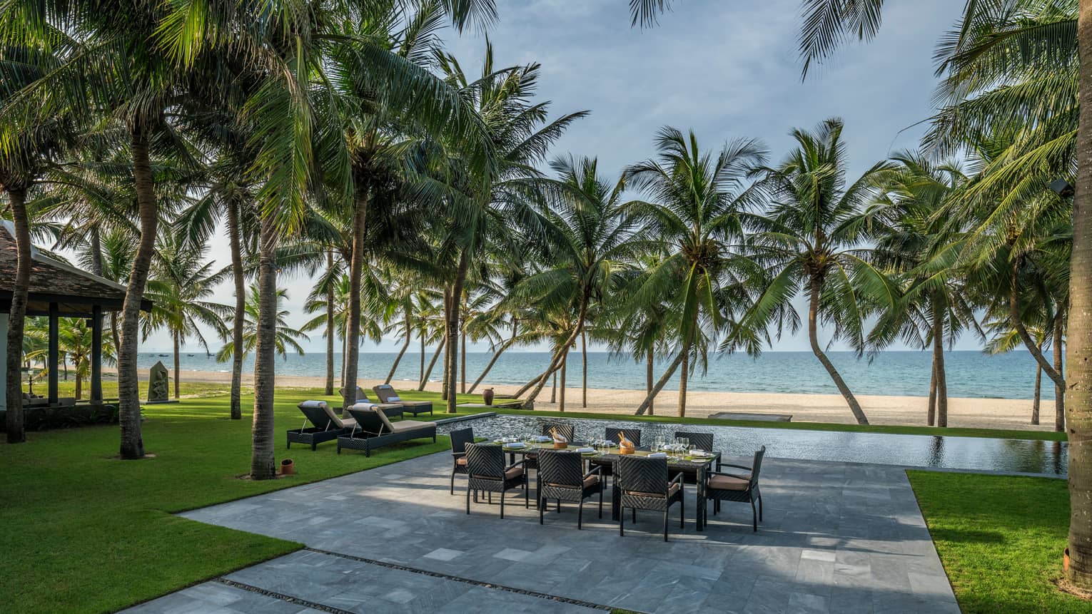 Beachfront Villa large stone patio with private dining table, lounge chairs under palms