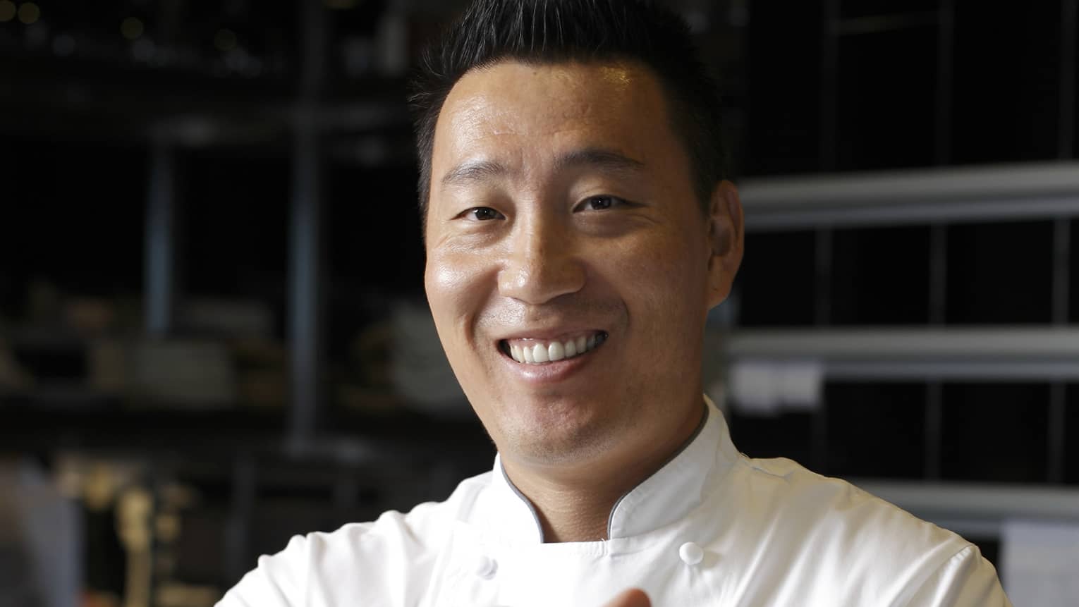Smiling chef presents a signature dish of tuna pizza garnished with slices of black truffle in a wide, white bowl.