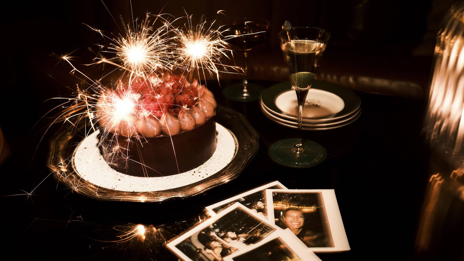 Sparkler candles in a chocolate cake and polaroid pictures nearby on a table