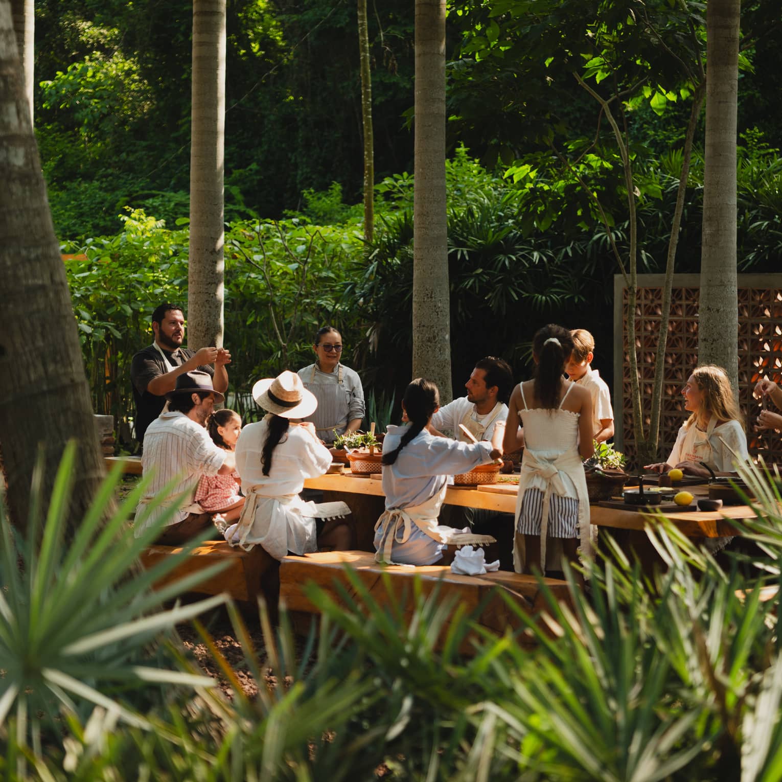 People seated around a long outdoor dining table set among palm trees