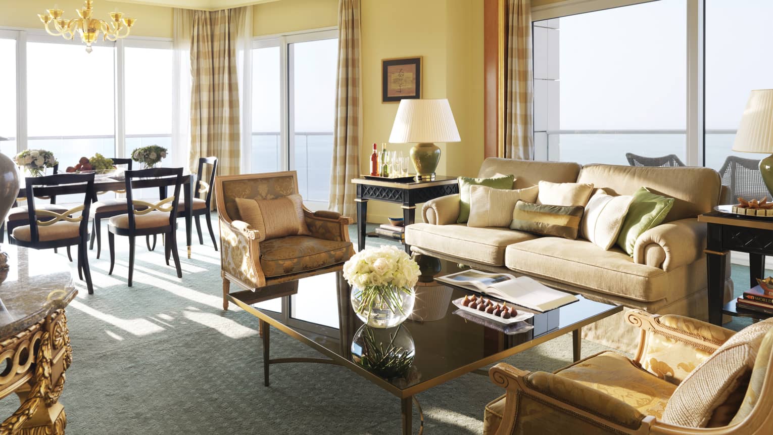 Premier Suite living room, beige sofa with green-and-gold pillows and elegant accent chairs, dining room in background