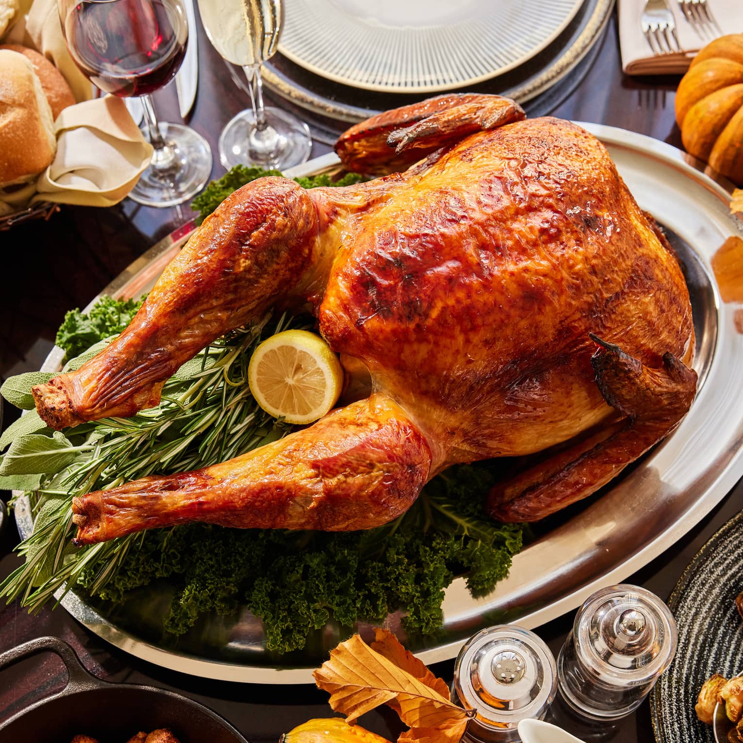 Dining table with a turkey, pumpkin, wine glasses and plates.