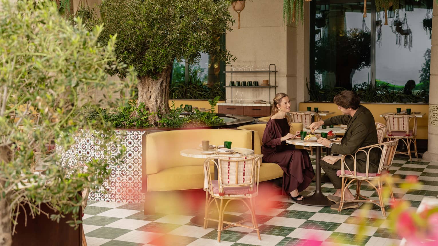 A couple dines at a colourful outdoor patio with green, checkered floors, mosaic tiles and lush greenery