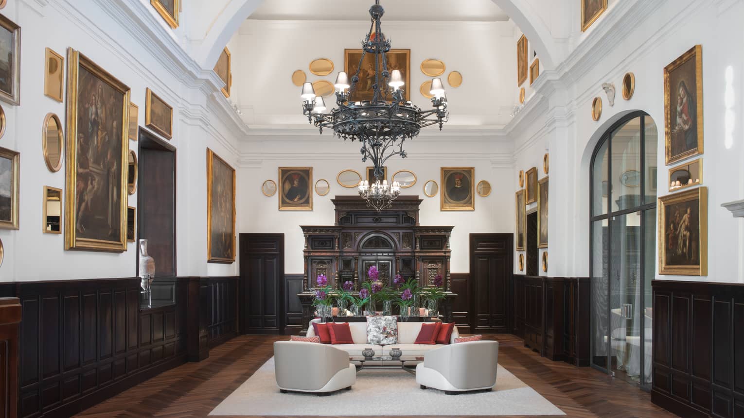Sala Museo with artwork lining both walls, white leather furniture, high ceilings, wrought iron chandelier, fireplace