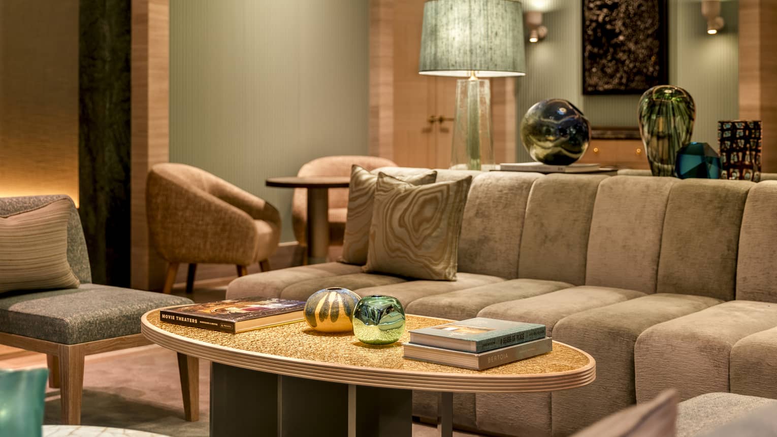 Lounge with beige sofa beside oval coffee table topped with large books and decor