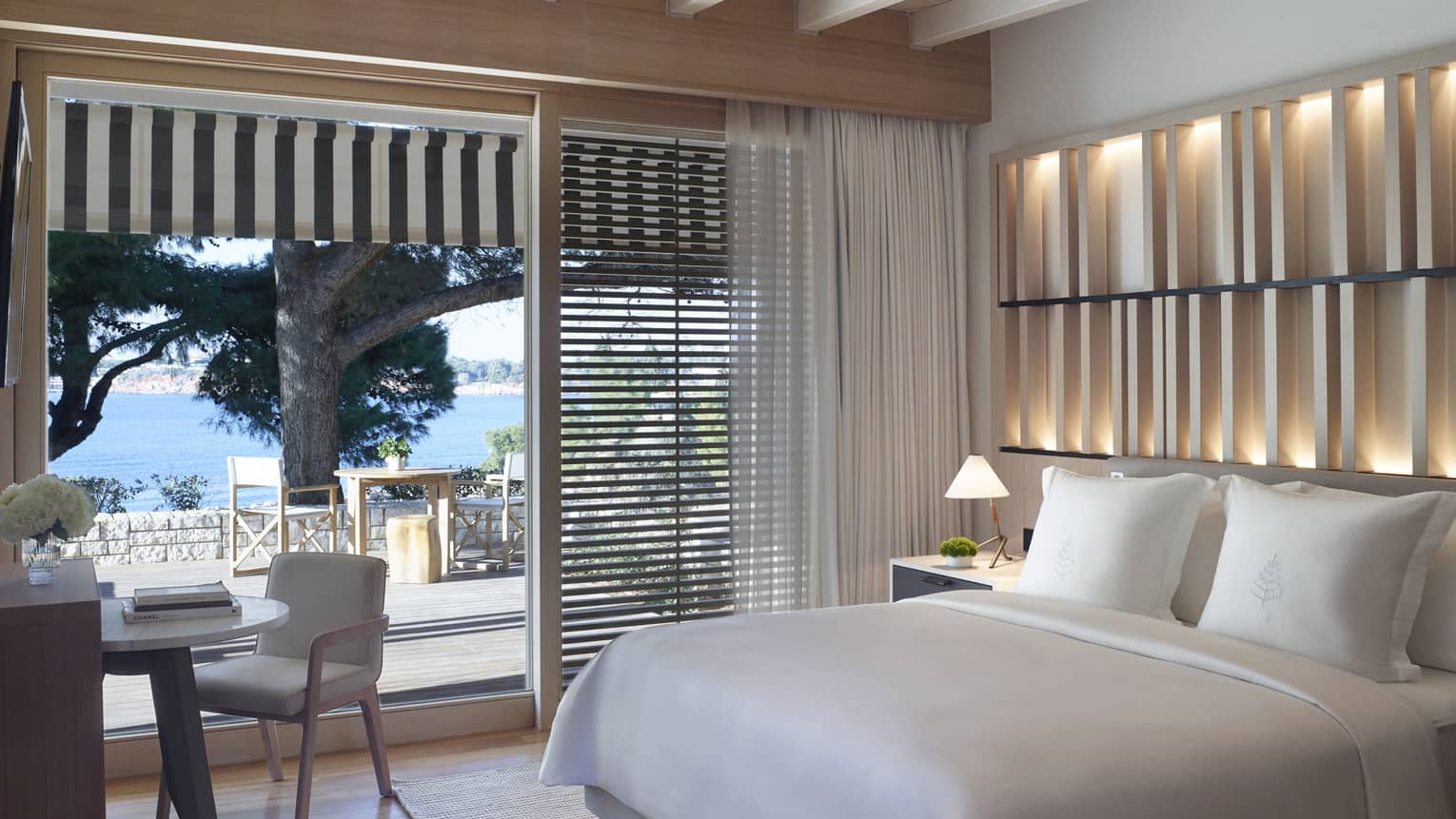 Bedroom with an illuminated wooden accent wall, white king bed, desk and chair, and sliding door to patio