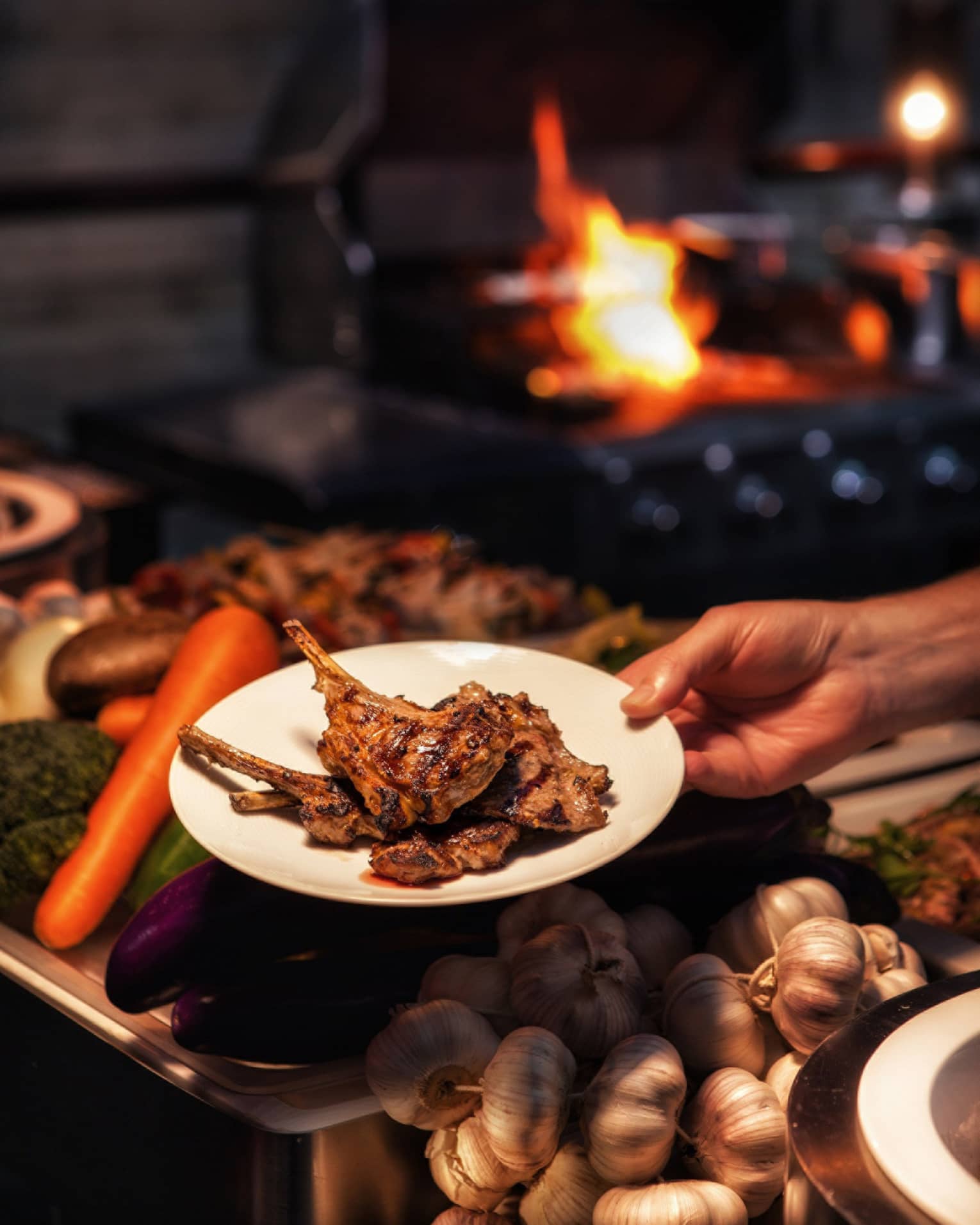 Hand holding barbecued chops on plate over fresh vegetables