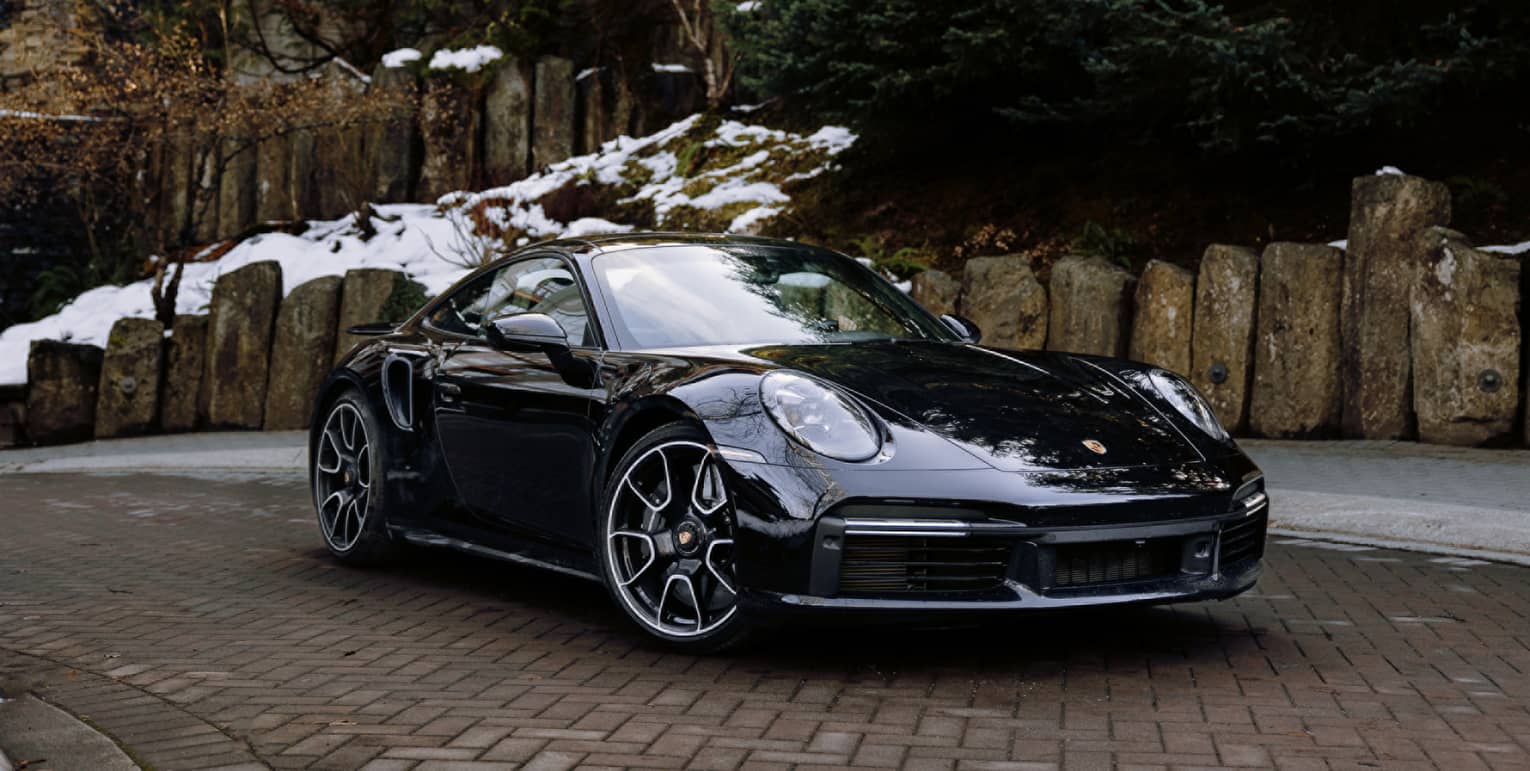Black Porsche coupe sits in brick driveway, snow on the ground behind it