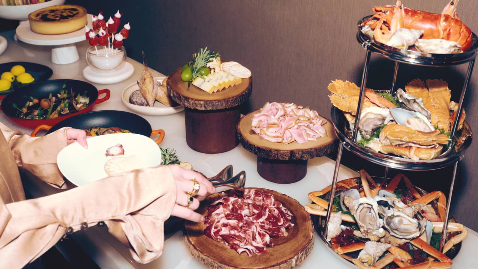 A person makes a plate at a buffet of gourmet food including a three-tier seafood tower