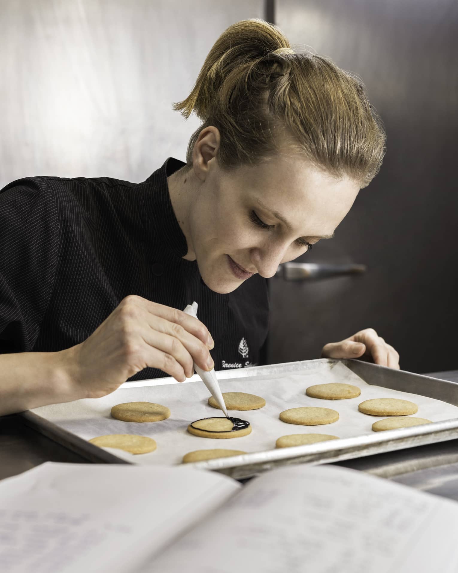 Pastry Chef adding chocolate garnish to row of cookies on baking pan