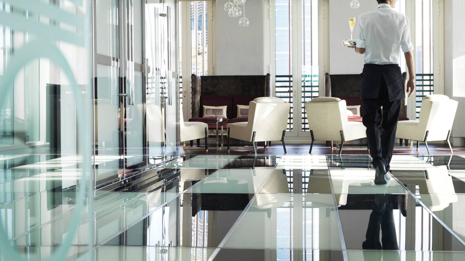 Back of server in uniform holding tray with champagne glass, shiny black-and-white checkered glass floors, walls