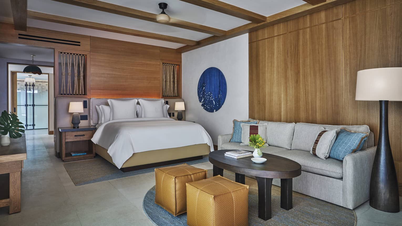 Luxury ocean-view casita suite interior with a bed, sofa seating area, wooden accents, decorative blue artwork and modern furnishings
