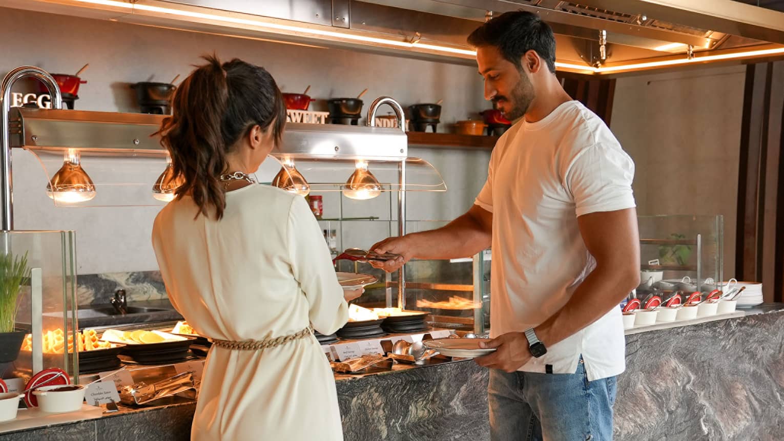 A man and woman stand serving their plates from a buffet station