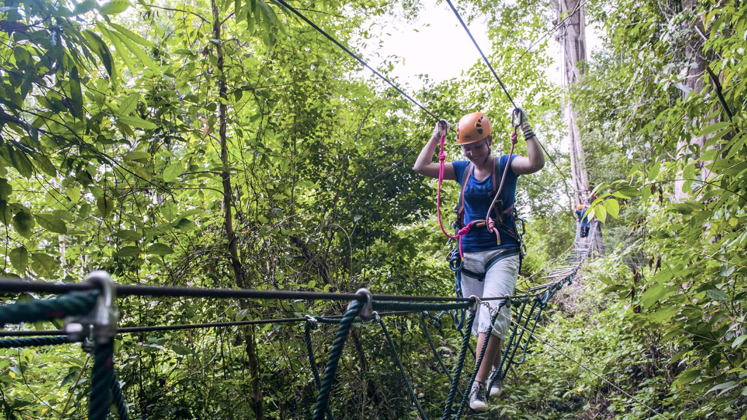 Woman wearing harness walks on ropes above trees