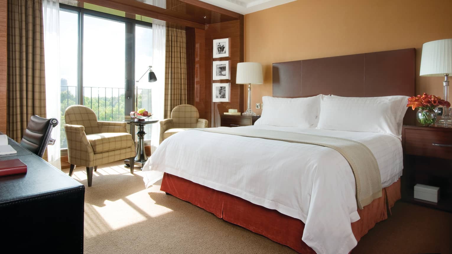 Premier Room bed with dark wood headboard, panel wall around sunny window, over armchair
