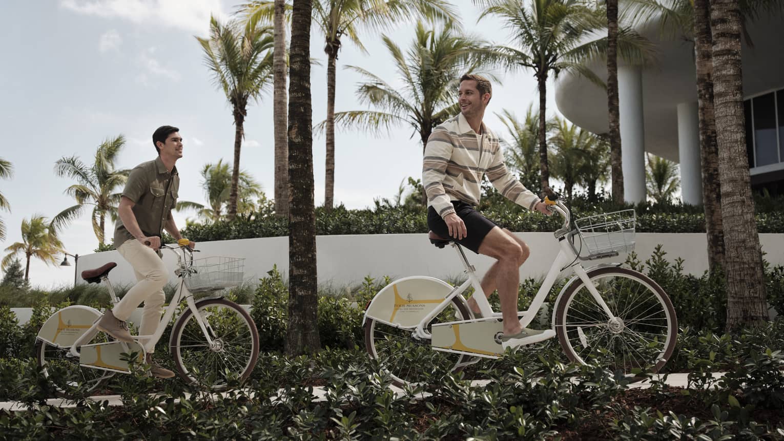 Two guests riding bikes on a sidewalk surrounded by palm trees