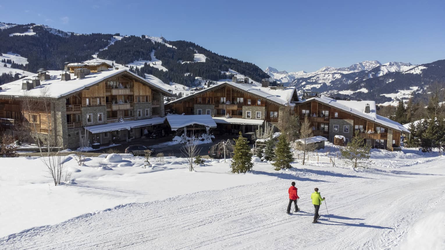 Two people show shoeing on snow-covered path in front of Four Seasons Hotel Megeve with Alps in backdrop