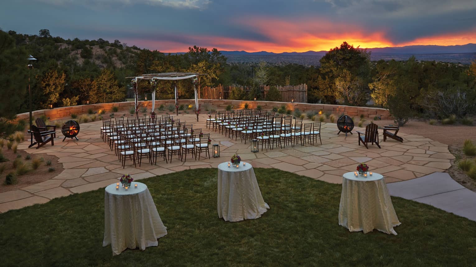 Rows of chairs on tiled surface facing wooden altar, cocktail tables overlooking trees and foothills at dusk