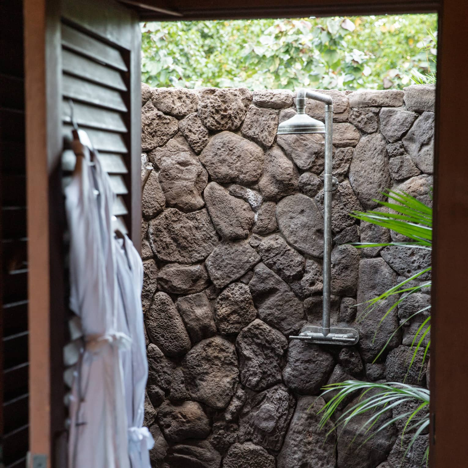 Two bathrobes hang on back of door to walk-out outdoor shower