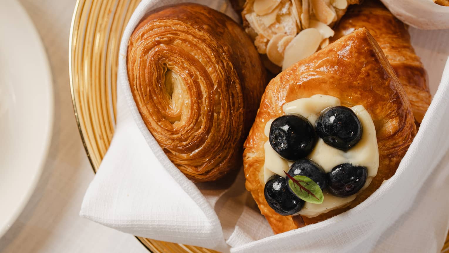 Gold-rimmed bowl filled with breakfast pastries sits on a table next to a white mug of coffee