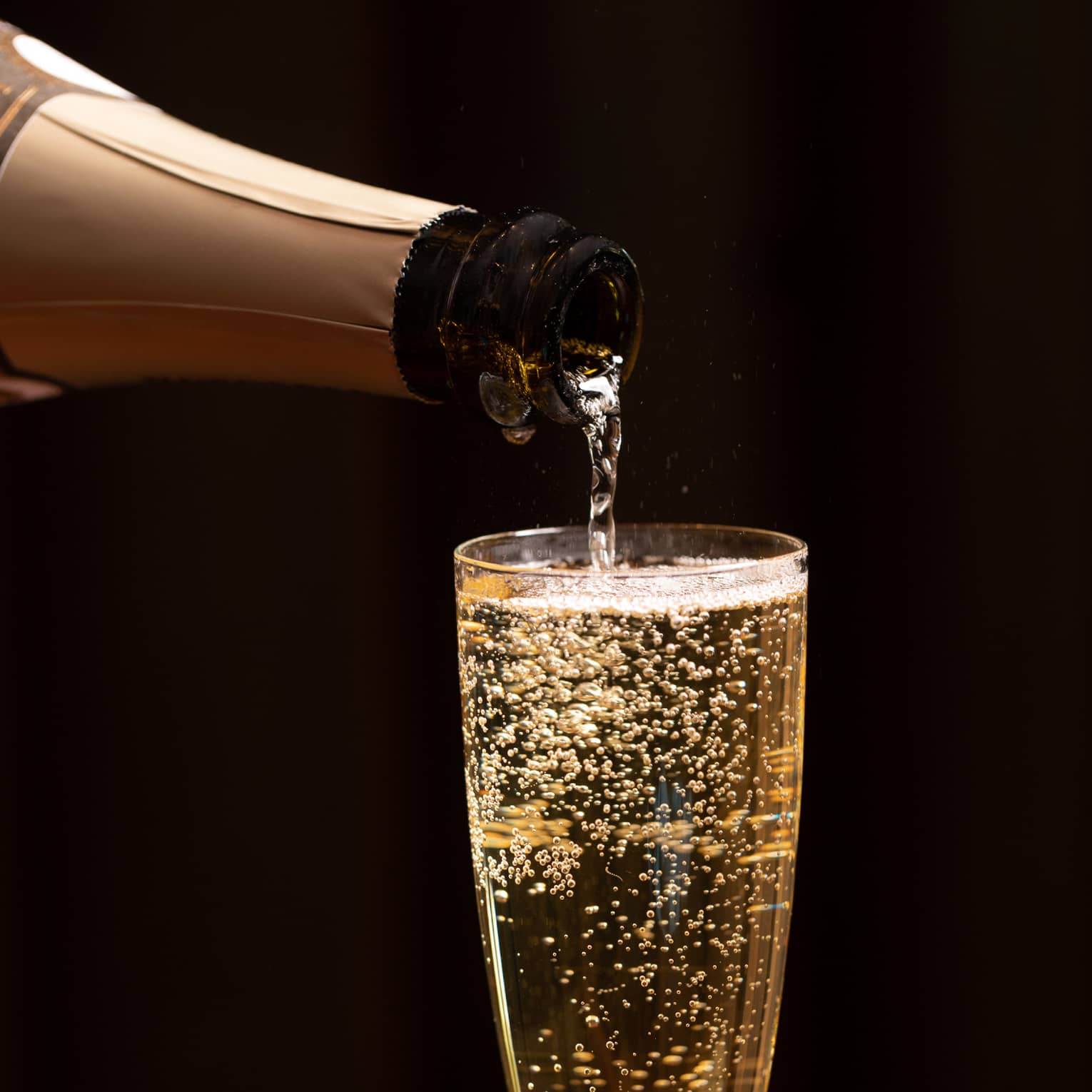 A bottle of champagne is poured into a glass as bubbles float to the top