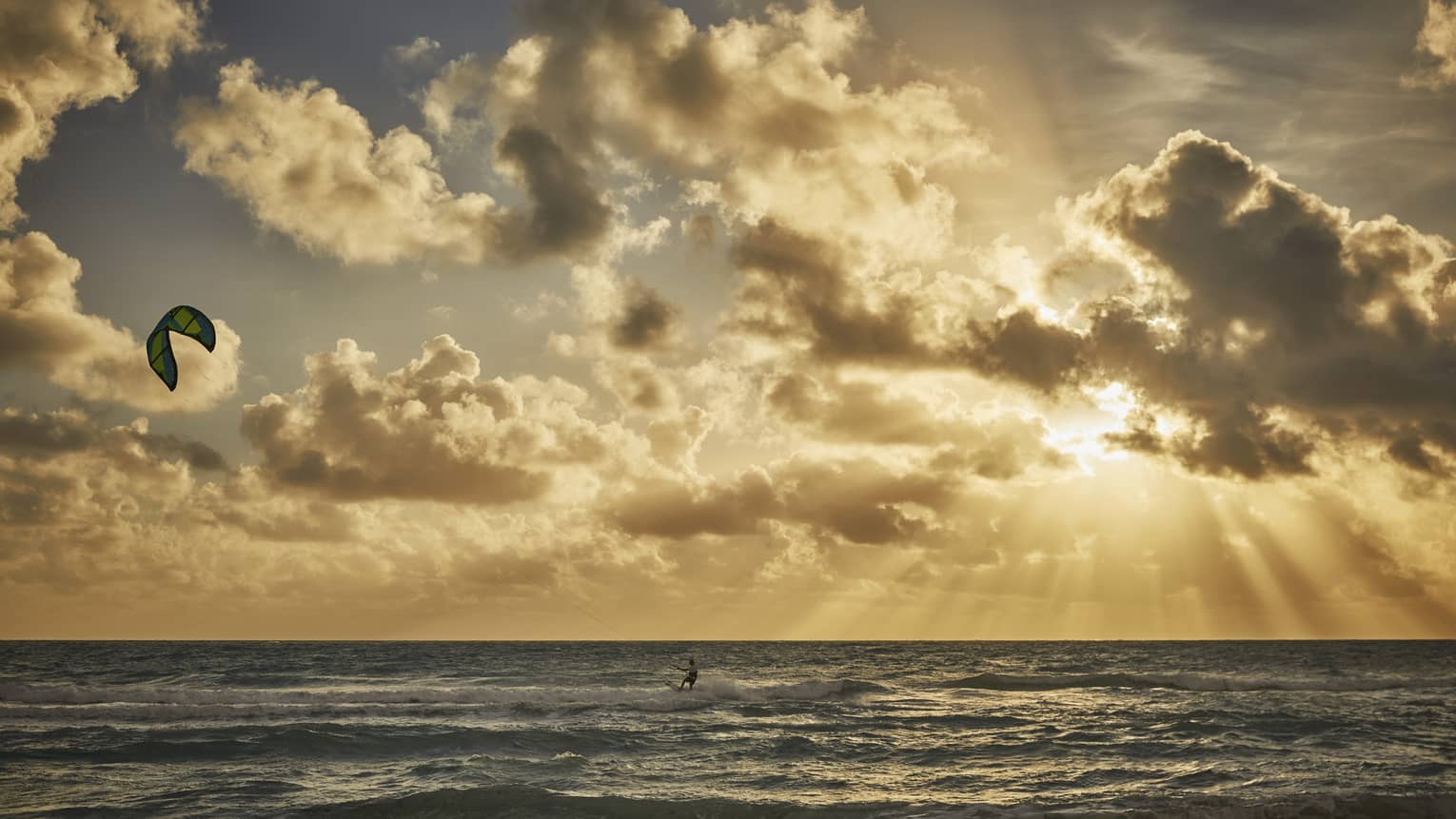 A four seasons guest windsurfs into the sunset over the ocean 