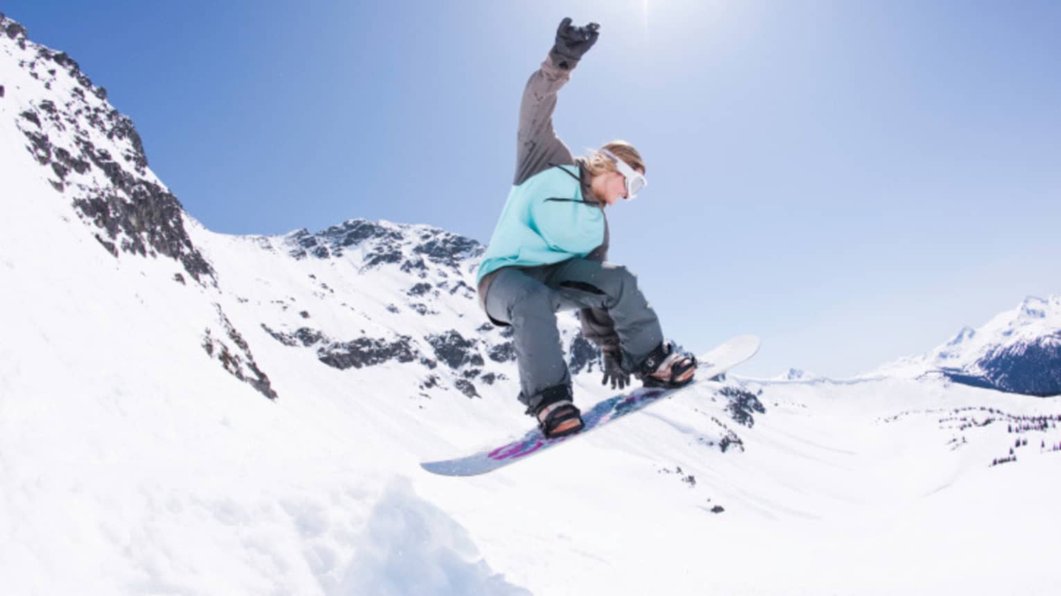 Snowboarder jumps, grabs board in mid-air on sunny mountain peak