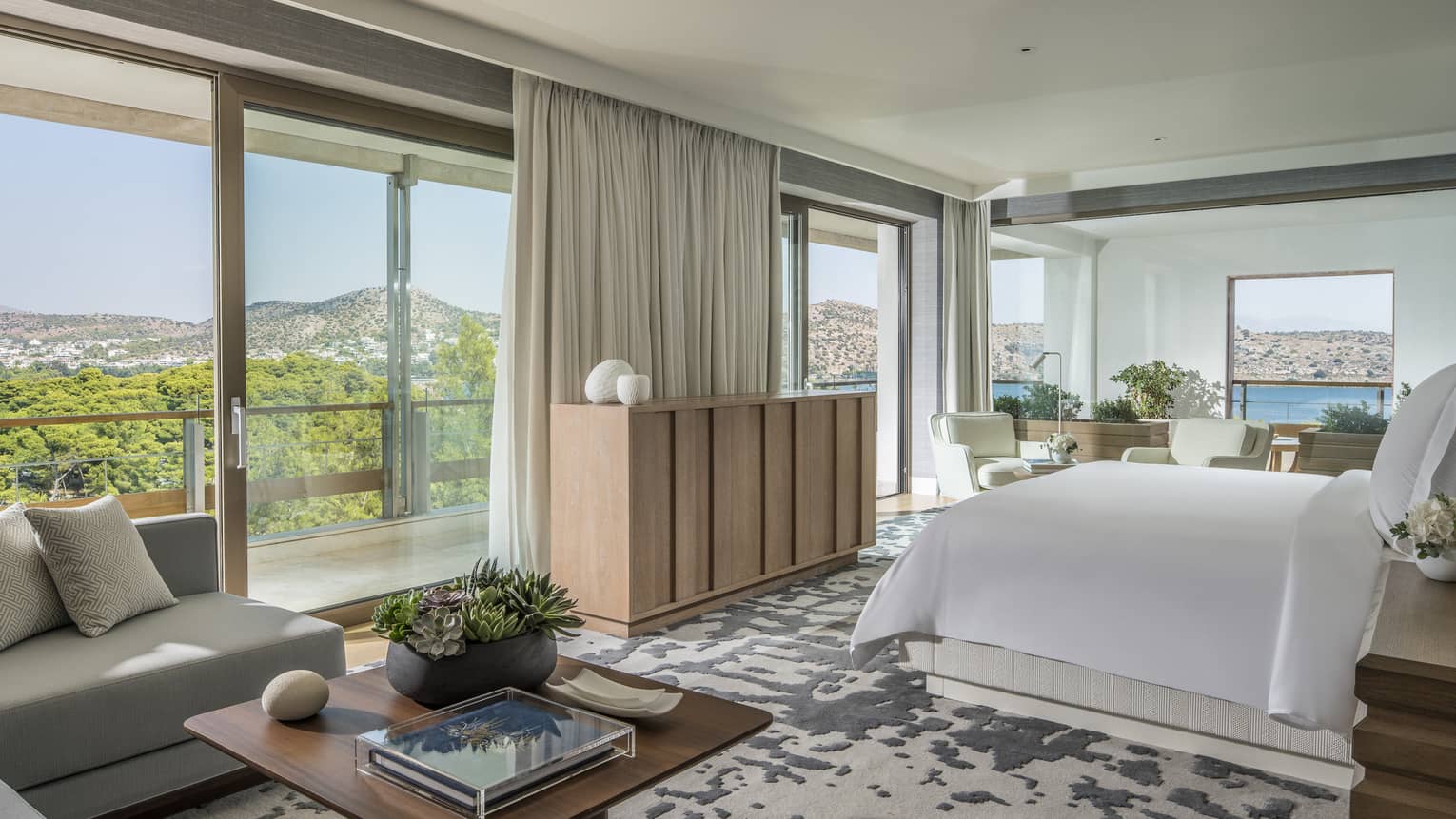 Arion Riviera Suite with white King bed, blonde wood sideboard, grey sectional sofa with square coffee table, panoramic ocean views
