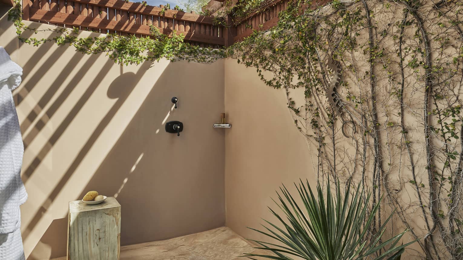 Stucco outdoor shower with creeping vines on the wall, covered by portico
