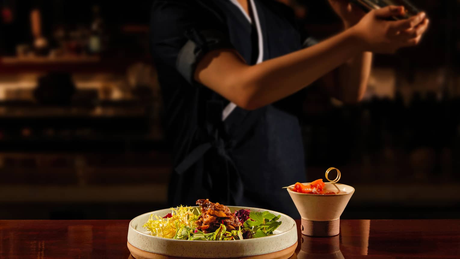 Bartender shaking a cocktail, bar bites at the forefront