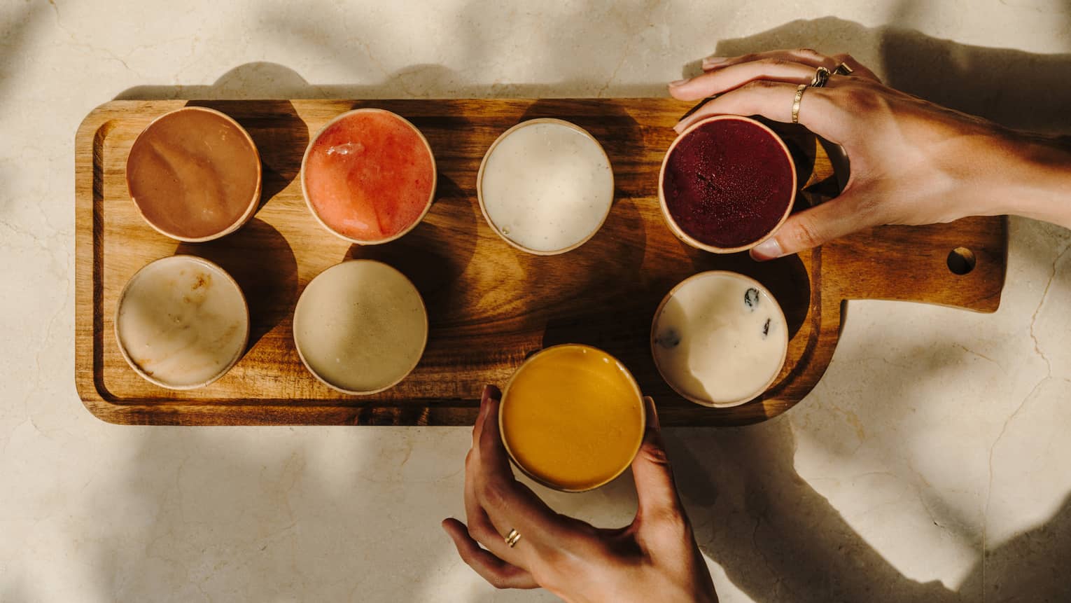 A person places eight cups of ice cream on a wood serving tray.