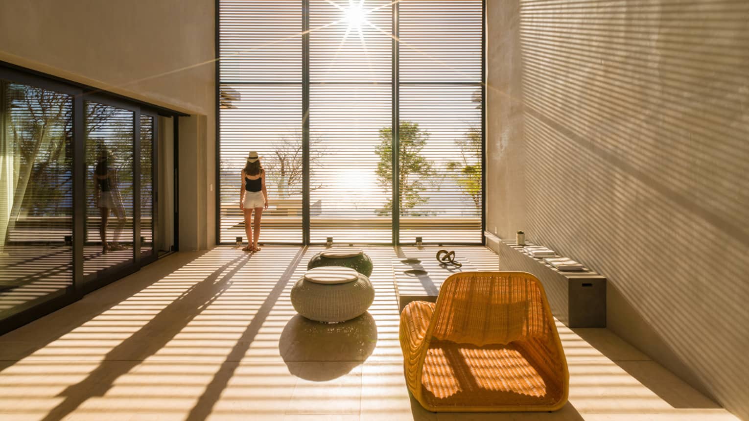 Woman stands by sunny floor to ceiling window in modern room
