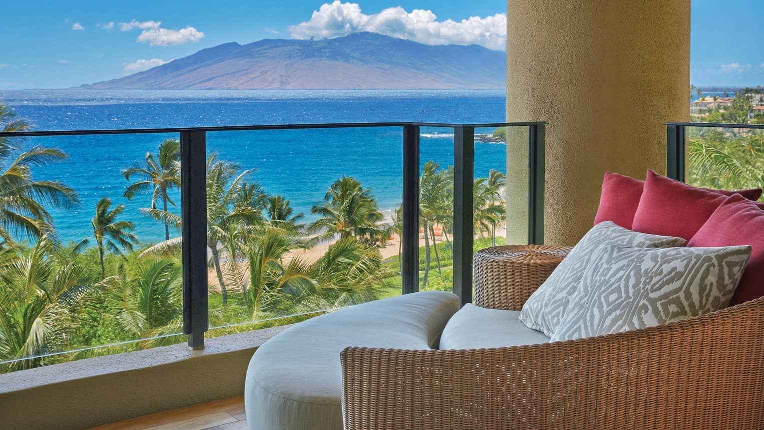 Cozy resort balcony with wicker seating and plush cushions, overlooking a tropical beach and ocean with a view of distant mountains