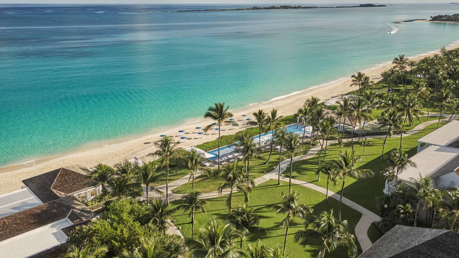 Bird?s eye view of a coast with bright ocean waters, white sand and palm trees on grass.