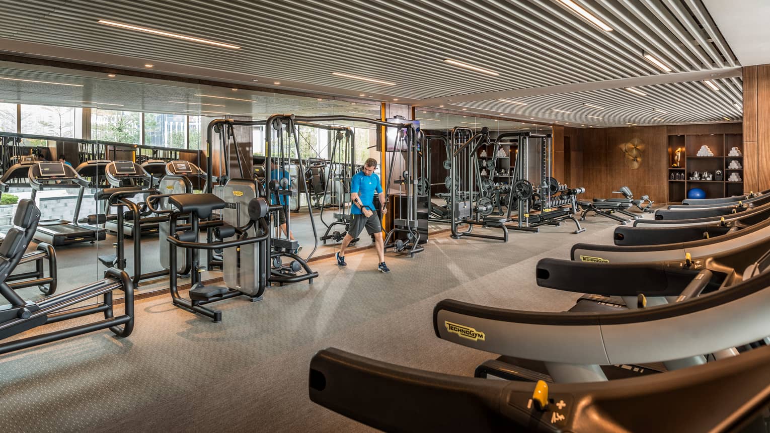 Man pulls weights machine in large Fitness Centre by mirror reflecting treadmills