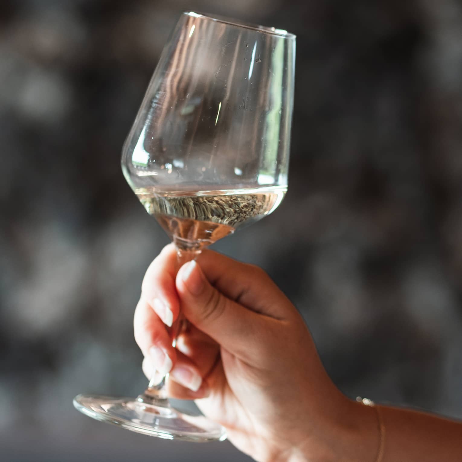 A hand lightly grips the stem of a glass of white wine, swirling it on a slight angle.