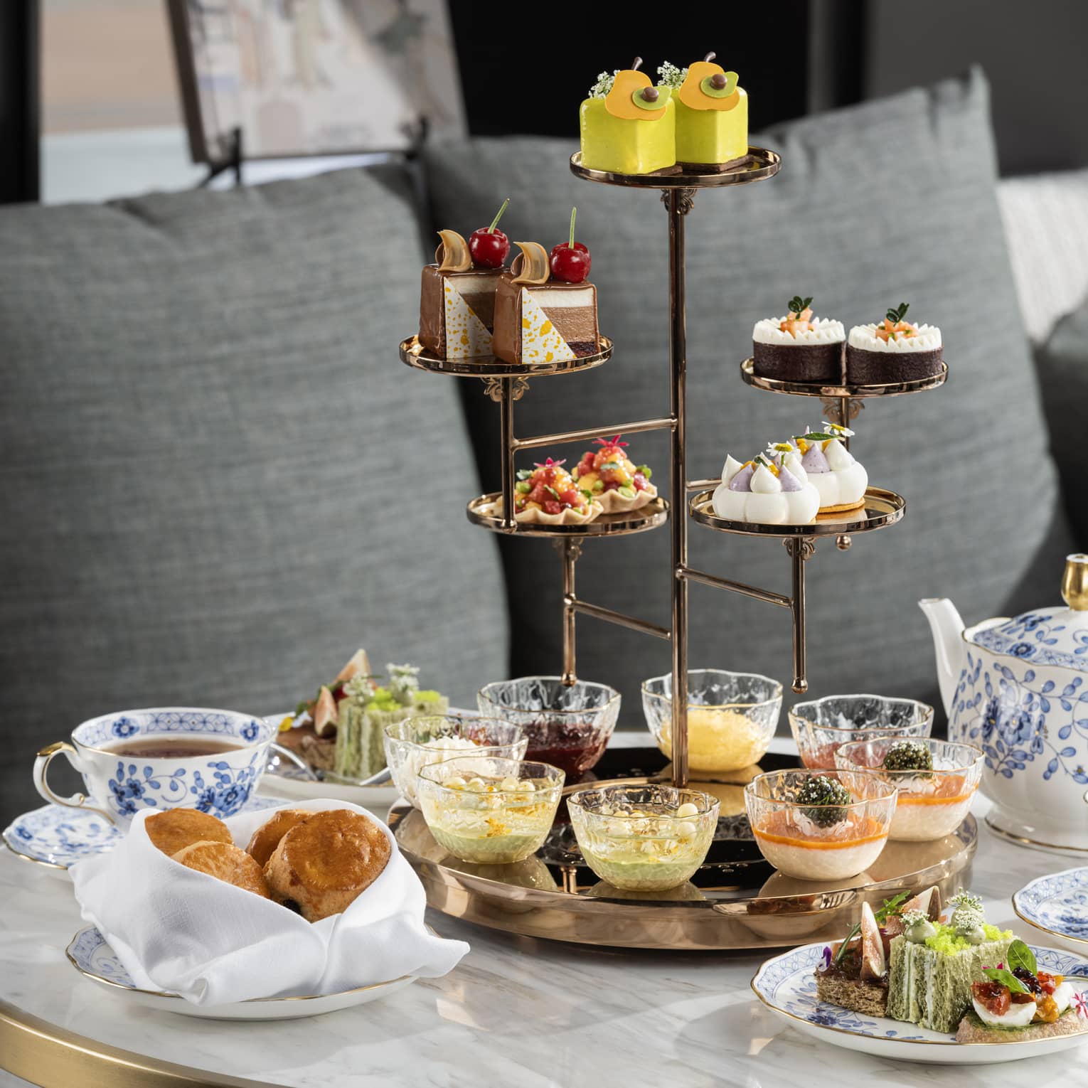 An artfully decorated array of desserts and spreads on a tiered tray, served with tea in elegant blue and white stoneware.