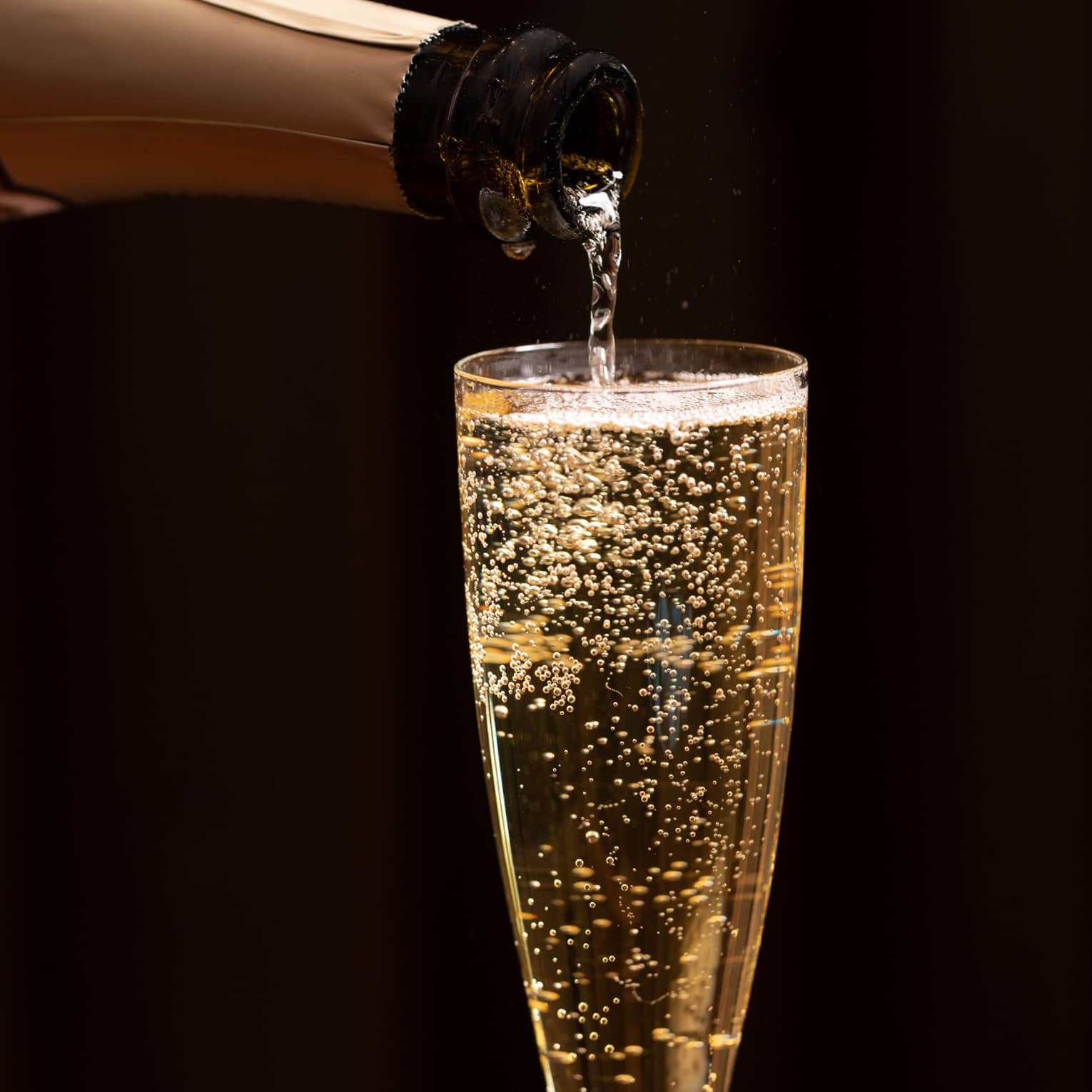 A bottle of champagne is poured into a glass as bubbles float to the top