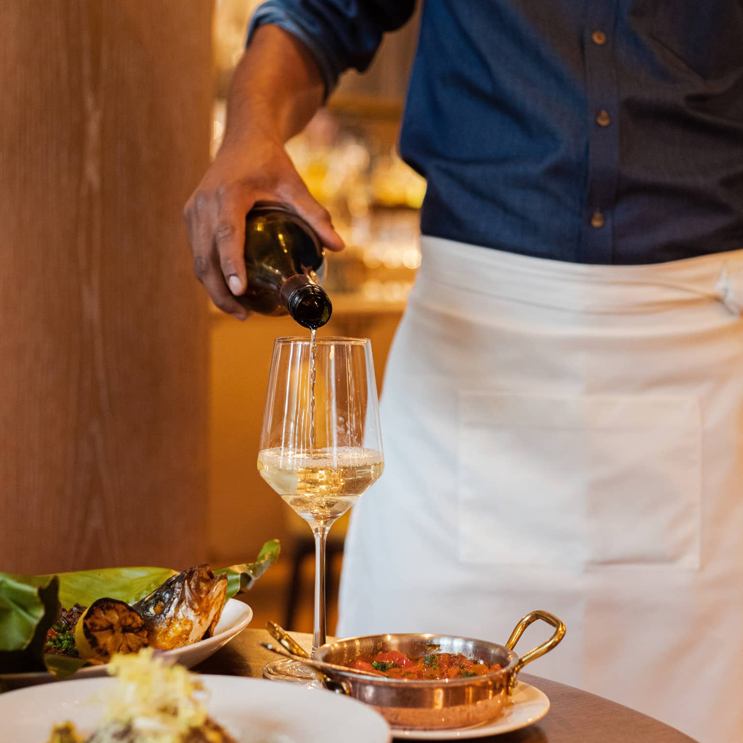 Roasted fish on a large leaf next to a glass of wine.
