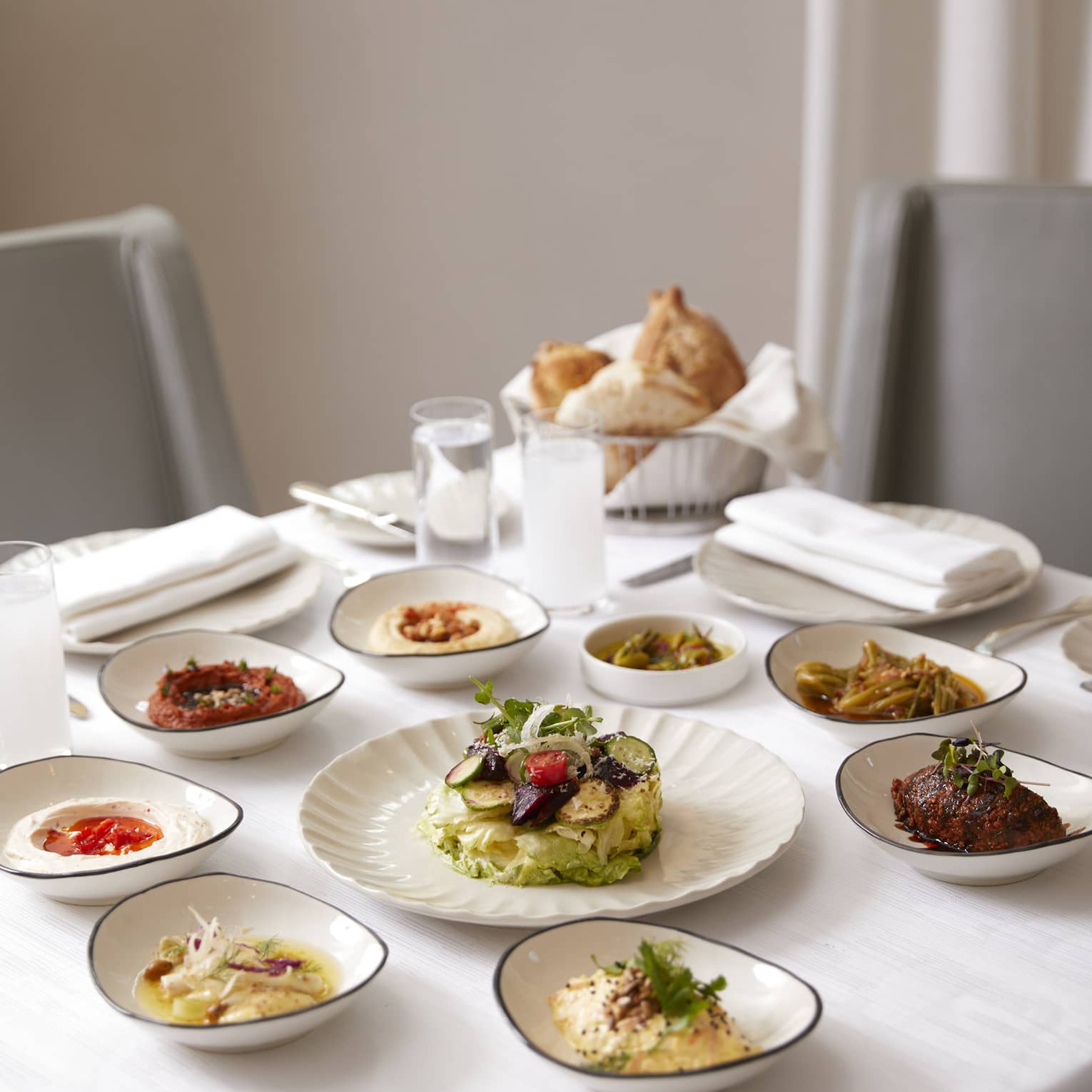 Small white dishes with meats, salads, sauces on small dining table