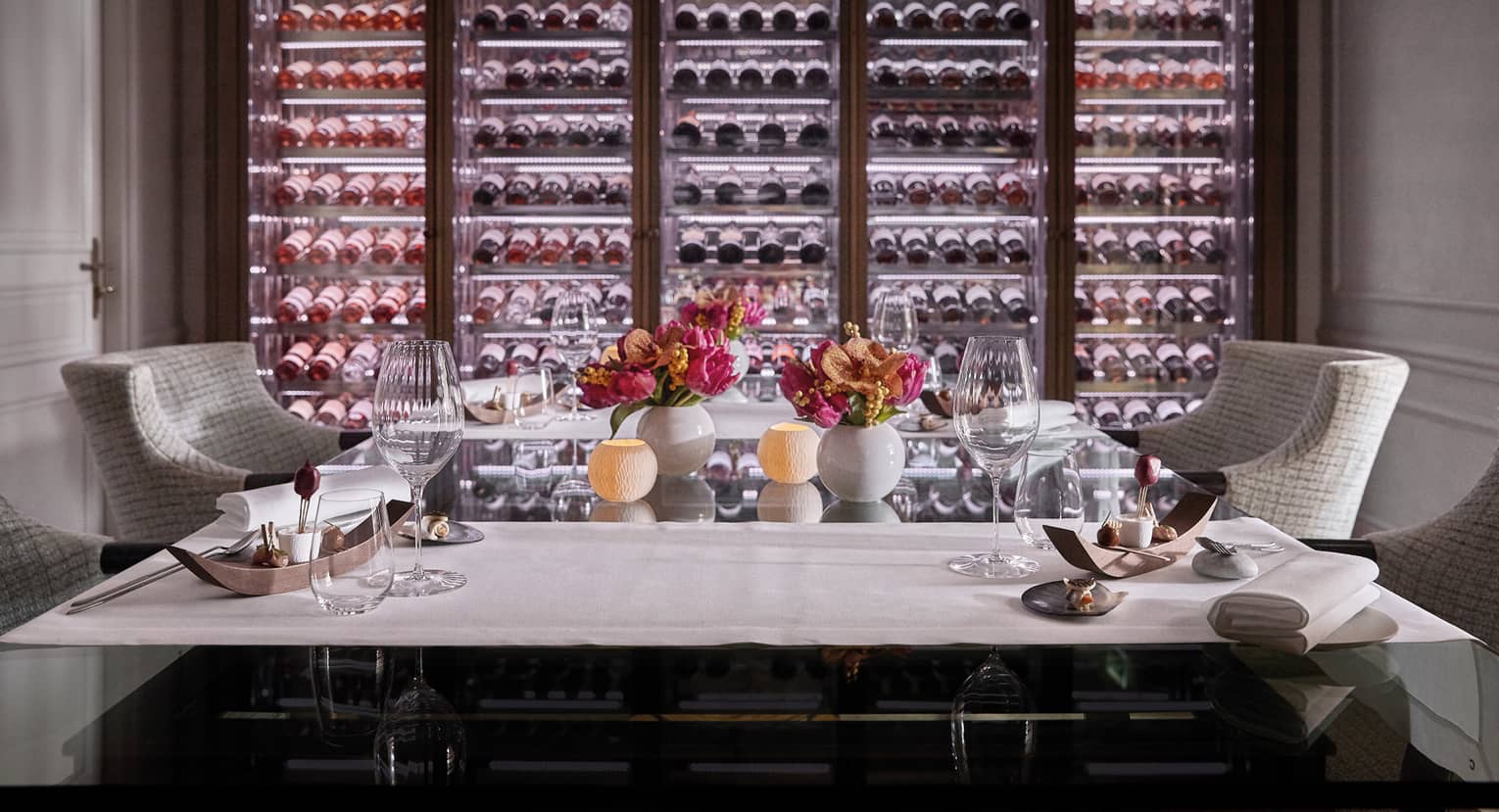 A private dining room with two chairs and an illuminated wall of wine on display