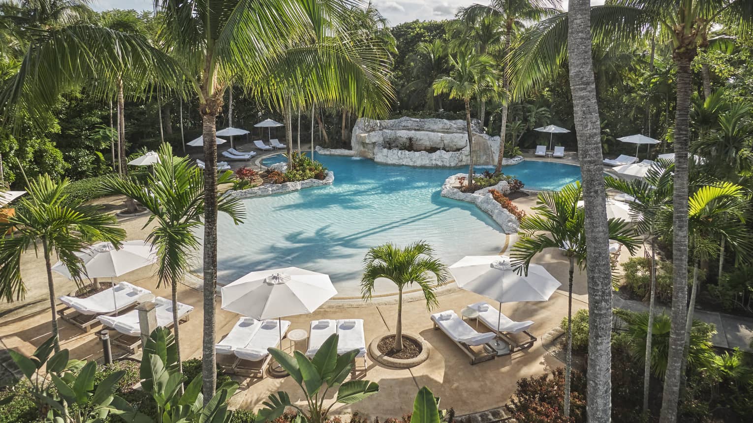 Luxury resort pool surrounded by palm trees, white lounge chairs and large umbrellas