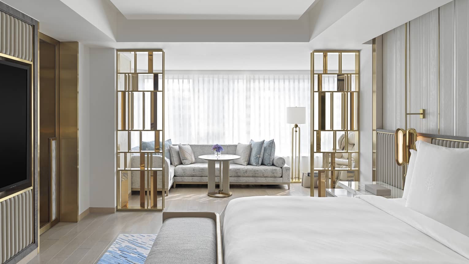 Dynasty Suite with King bed, gold accents and decor, white sofa with light blue pillows, natural lighting