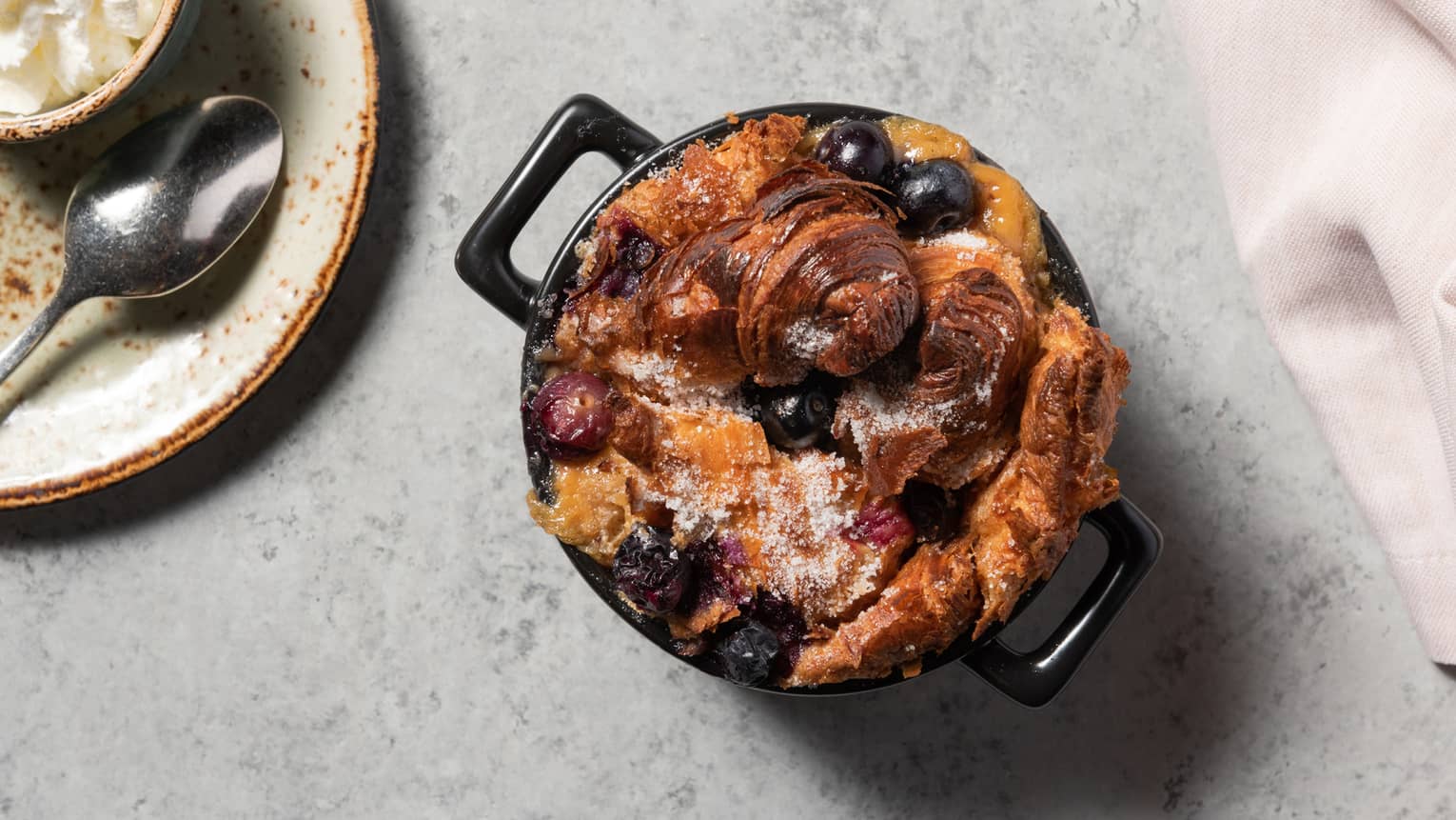 A bread pudding with blueberries in a black bowl.