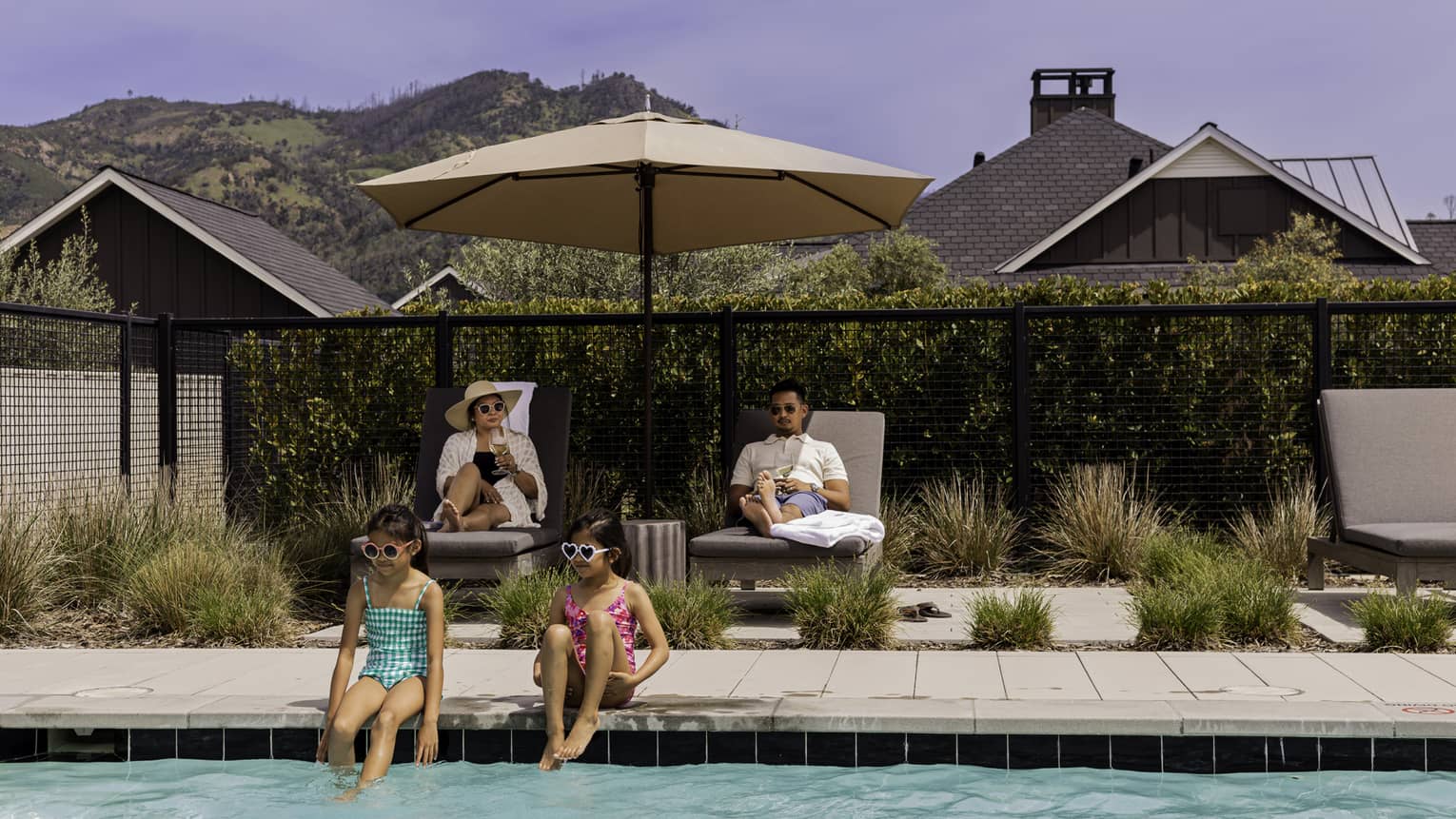 Two guests sitting on lounge chairs while the other two guests sit near the pool.