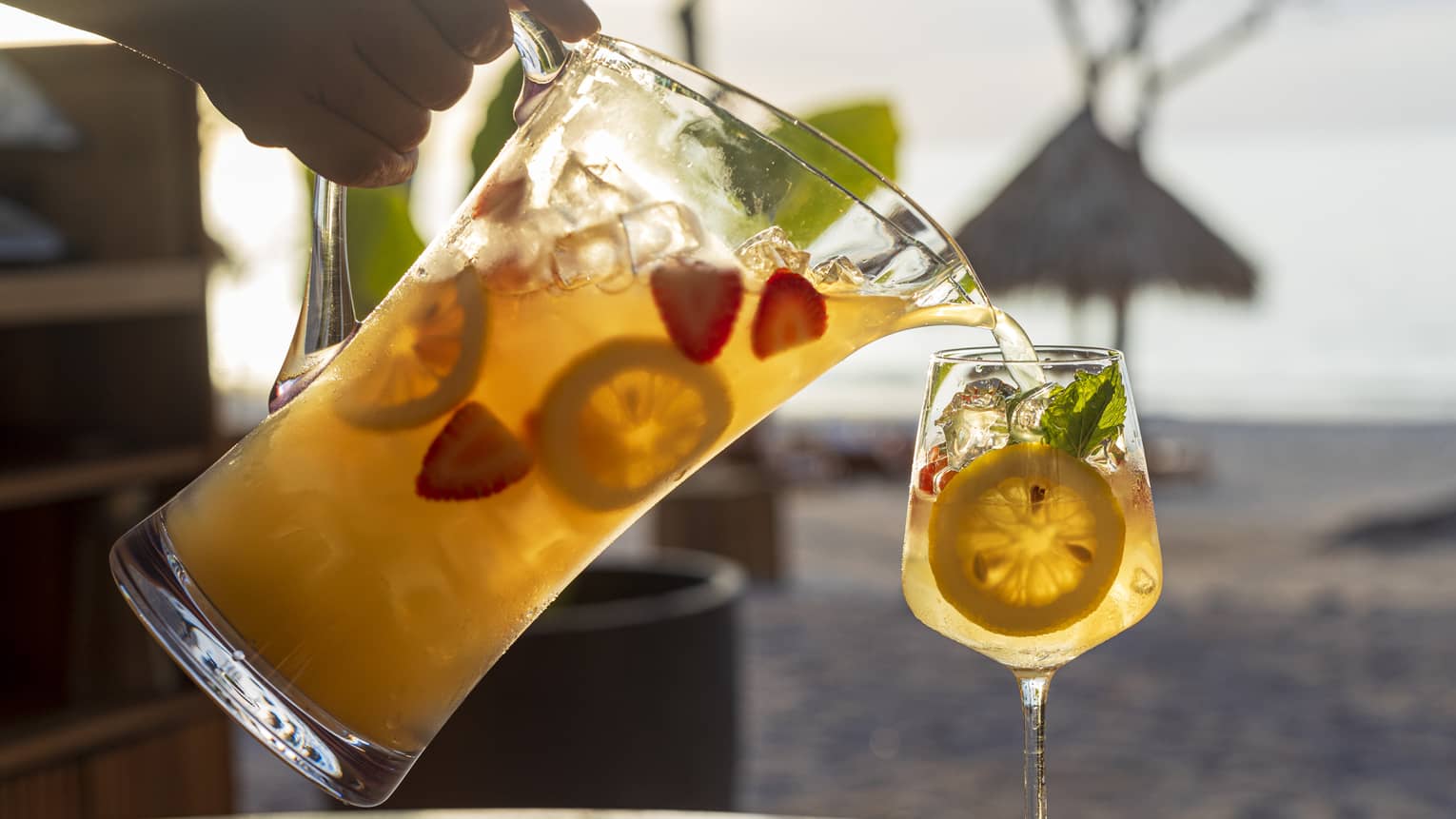 Hand pouring from a pitcher of white sangria into a tall glass