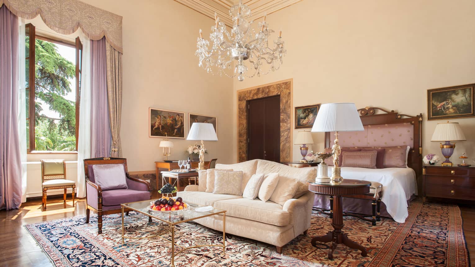 Gallery Suite white sofa, purple armchair, bed under large crystal chandelier, high ceiling