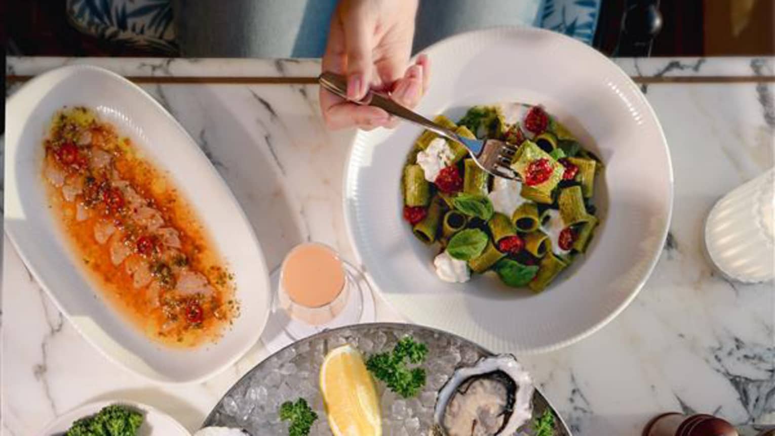 Aerial view of a white marble dining table topped with chilled oysters, colourful salads and cocktails