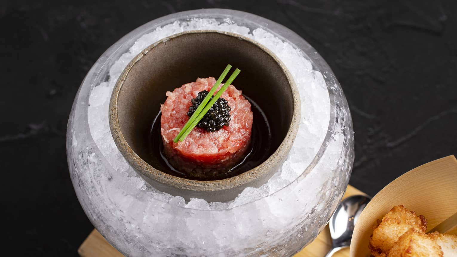 Small serving of tuna tartare topped with caviar plated in a rounde stone bowl surrounded by ice