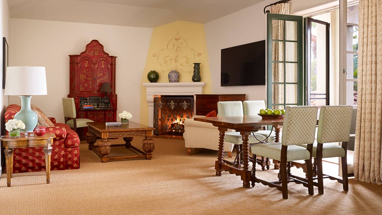 Bright Santa Cruz Suite with red silk sofa, carved wood table by fireplace, table, French doors